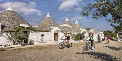 People ride bicycles past the white trulli houses of Alberobello, Puglia, Italy